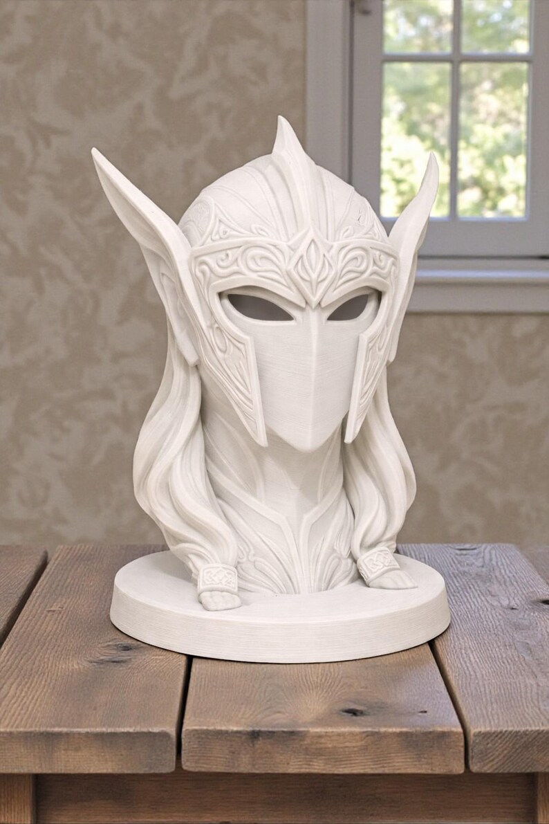 May include: A white sculpture of a helmeted figure with long hair and detailed facial features. The helmet has ornate patterns and pointed extensions. The sculpture sits on a round base, displayed on a wooden table.