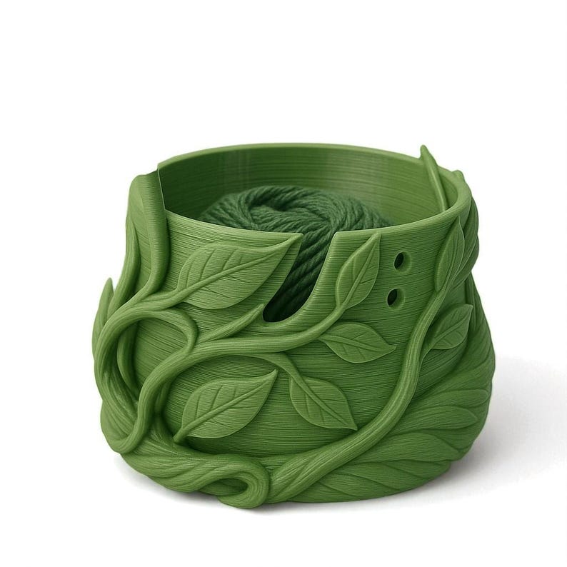 May include: A green yarn bowl with a leaf design. The bowl is filled with green yarn. The exterior of the bowl is decorated with detailed, three-dimensional leaves and vines.