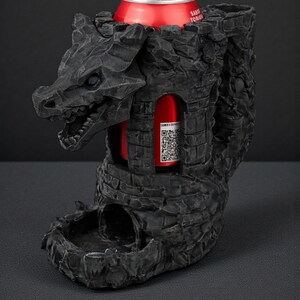 May include: A black dragon-shaped can holder with a red can inside. The holder has a detailed, textured design resembling a castle. The dragon's head is at the top, and the can is visible through an opening.