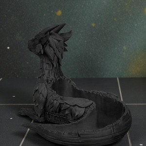 May include: A black dragon-shaped decorative bowl. The dragon has detailed features, including horns, leaf-like accents, and a coiled body forming the bowl. The bowl is sitting on a dark surface.