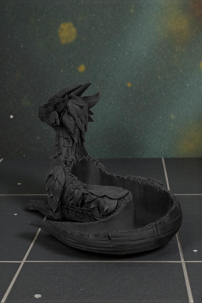 May include: A black dragon-shaped decorative bowl. The dragon has detailed features, including horns, leaf-like accents, and a coiled body forming the bowl. The bowl is sitting on a dark surface.