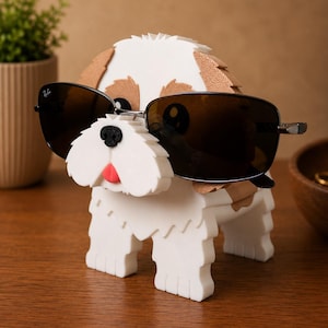 May include: A white and brown dog-shaped sunglasses holder with black sunglasses. The dog has a red tongue and a black nose. The sunglasses have a silver frame. The holder is on a wooden surface.