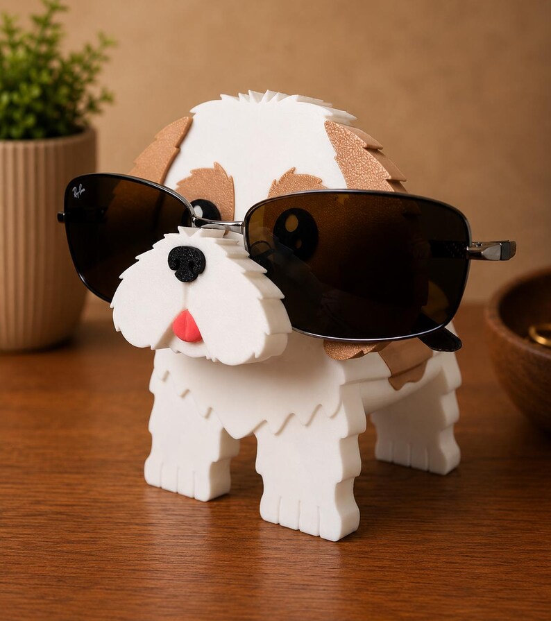 May include: A white and brown dog-shaped sunglasses holder with black sunglasses. The dog has a red tongue and a black nose. The sunglasses have a silver frame. The holder is on a wooden surface.