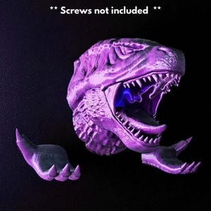May include: A purple dinosaur head with an open mouth and sharp teeth, and two detached clawed hands. The text "** Screws not included **" is above the dinosaur head. The image is set against a black background.