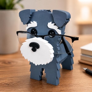 May include: A blue and white dog-shaped eyeglasses holder with black-framed glasses. The dog has a white beard and eyebrows, and black eyes and nose. The holder is made of layered material and sits on a wooden surface.