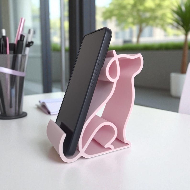 May include: A pink dog-shaped phone stand holds a black smartphone. The stand is made of a solid material and has a smooth finish. The phone is positioned vertically, resting against the stand's back and base.