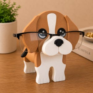 May include: A whimsical dog-shaped eyeglasses holder in brown, white, and black. The holder features a cartoon-like design with large eyes and a white snout. The dog is wearing a pair of black-framed glasses. A charming and functional desk accessory.