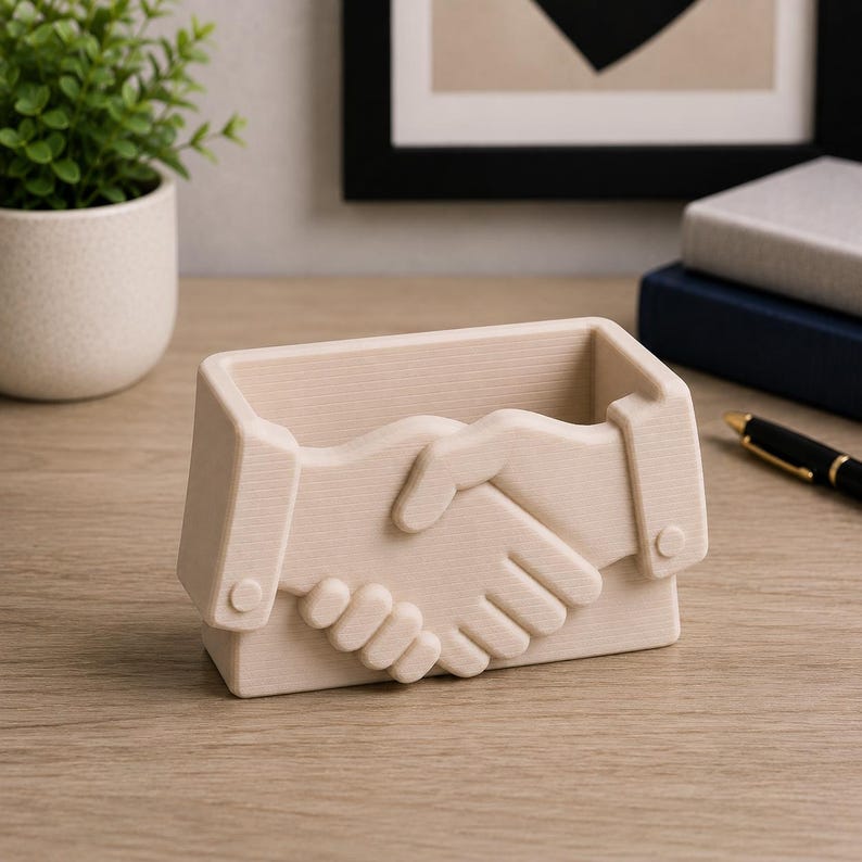 May include: Beige desk organizer shaped like two hands shaking. The organizer has a rectangular base and a hollow interior for storing pens, pencils, or other office supplies. The design features detailed relief of clasped hands.