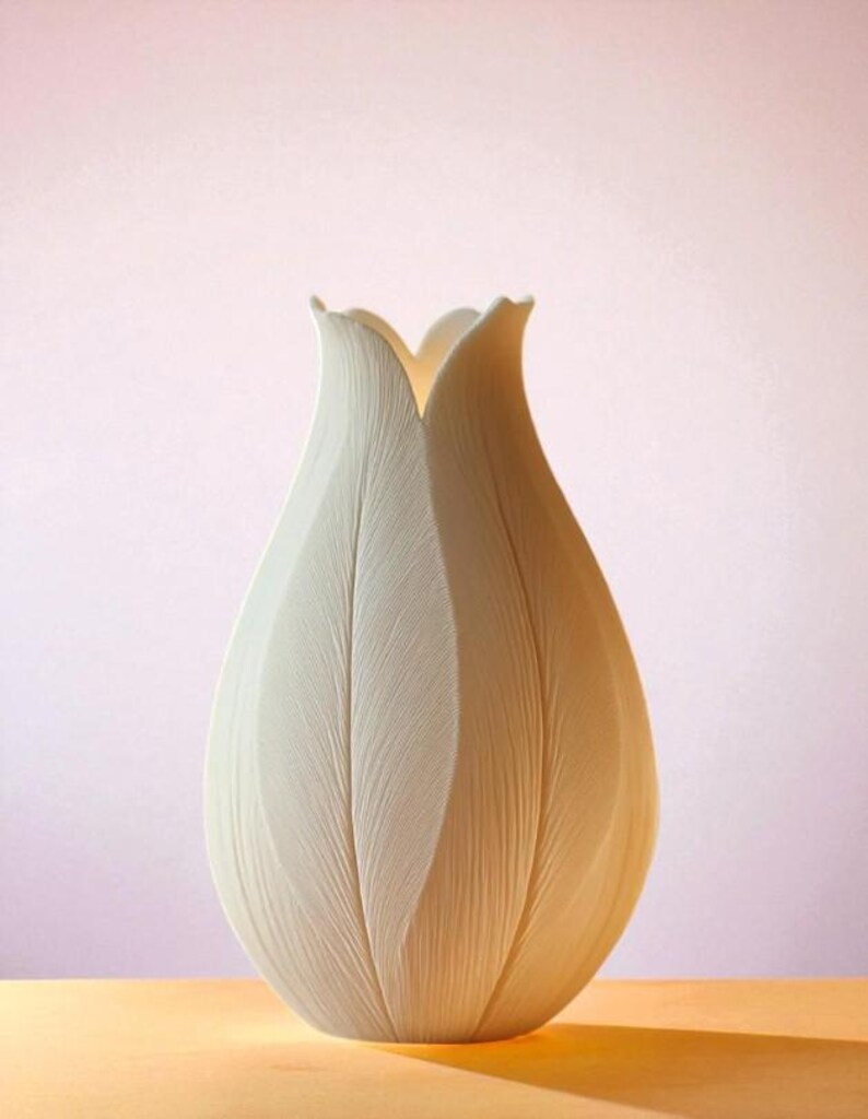May include: A white, tulip-shaped vase with a textured surface. The vase has a wide, rounded base that tapers upwards, with petal-like edges at the top. The vase is set against a soft pink background and a yellow surface.