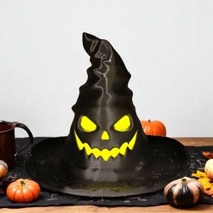 May include: A black Halloween witch's hat with a carved jack-o'-lantern face, featuring glowing yellow eyes and a toothy grin. The hat is displayed on a wooden table with pumpkins and autumn leaves, creating a festive seasonal display.