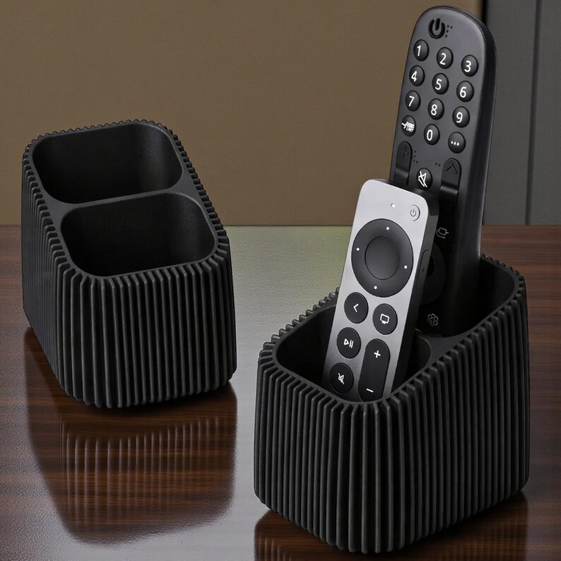 May include: Two black ribbed remote control organizers. One organizer has two compartments, the other has three compartments and holds two remotes. The remotes are black and silver.