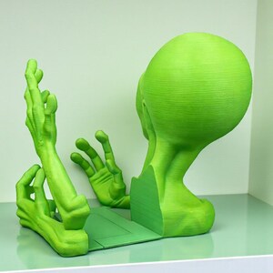 May include: A green alien-themed bookend set. The bookend features a stylized alien head and hands, all in a vibrant green color. The design is modern and unique, perfect for adding a touch of whimsy to any bookshelf.