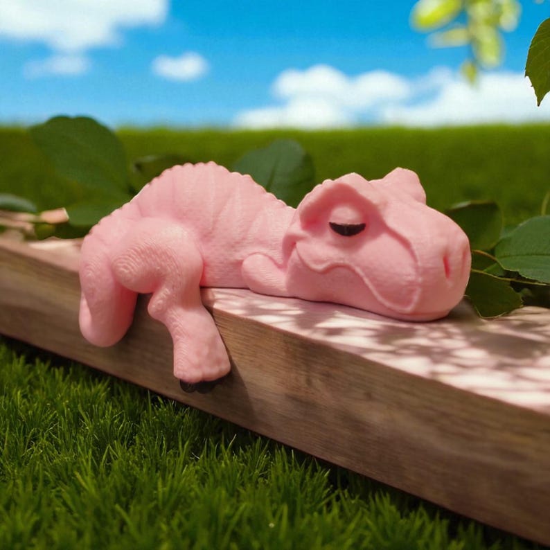 May include: A light pink dinosaur figure resting on a wooden surface. The dinosaur is lying down with its eyes closed. The background features green grass and a blue sky with clouds. The figurine is a solid, smooth colour.