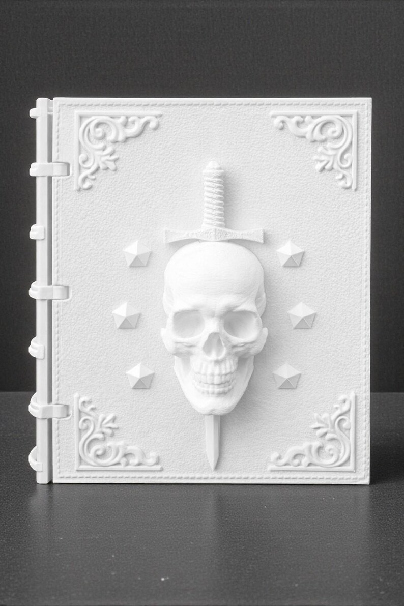 Peut inclure: Un livre blanc textur&eacute; avec un design de cr&acirc;ne et d'&eacute;p&eacute;e. Le cr&acirc;ne est centr&eacute;, avec une &eacute;p&eacute;e qui le transperce. Des accents d&eacute;coratifs d'angle et des formes g&eacute;om&eacute;triques entourent le cr&acirc;ne. Le livre a une tranche avec des charni&egrave;res.