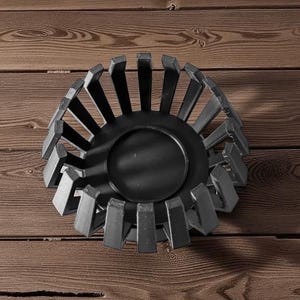 Puede incluir: Un cuenco decorativo de metal negro con base circular y soportes rectangulares verticales. El cuenco se encuentra sobre un fondo de madera, creando un contraste de texturas y tonos. El dise&ntilde;o es moderno y geom&eacute;trico.