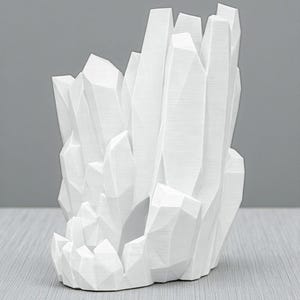 May include: A white, geometric crystal sculpture with a cluster of sharp, angular forms. The sculpture has a textured surface and is set against a neutral gray background. The design resembles a geode or a cluster of crystals.