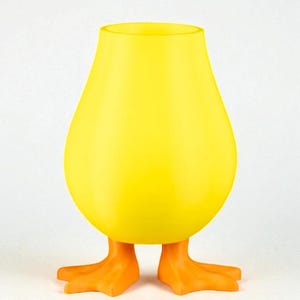 Puede incluir: Un jarr&oacute;n amarillo caprichoso con forma de pato, con un cuerpo redondeado y una parte superior abierta. El jarr&oacute;n tiene patas de pato naranjas como base, creando un art&iacute;culo decorativo l&uacute;dico y &uacute;nico. El color amarillo brillante es llamativo.