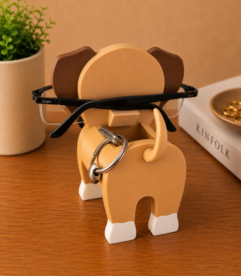 Peut inclure: Un organiseur de bureau fantaisiste en forme de chien, de couleur beige et marron, avec des accents blancs sur les pieds. L'organisateur contient une paire de lunettes &agrave; monture noire et un jeu de cl&eacute;s. Une petite plante en pot et un livre sont en arri&egrave;re-plan.