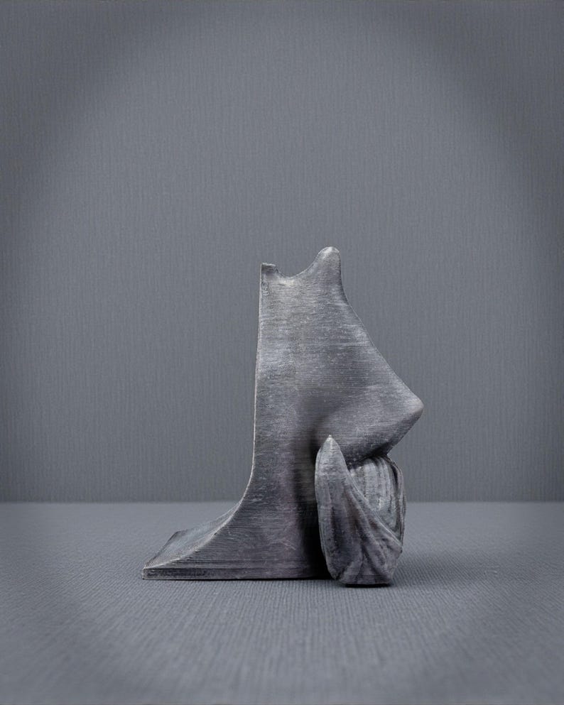 May include: A gray sculpture of a human profile, featuring a nose and a hand resting near the face. The sculpture has a textured surface and is set against a gray backdrop. The artwork is a unique decorative piece.
