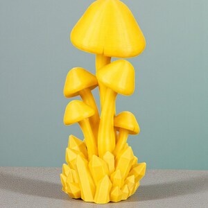 K&ouml;nnte beinhalten: Eine leuchtend gelbe Pilzskulptur mit mehreren Pilzkappen und -stielen, auf einem Sockel aus gelben kristallartigen Formationen. Es handelt sich um einen Dekorationsartikel, wahrscheinlich f&uuml;r die Inneneinrichtung.