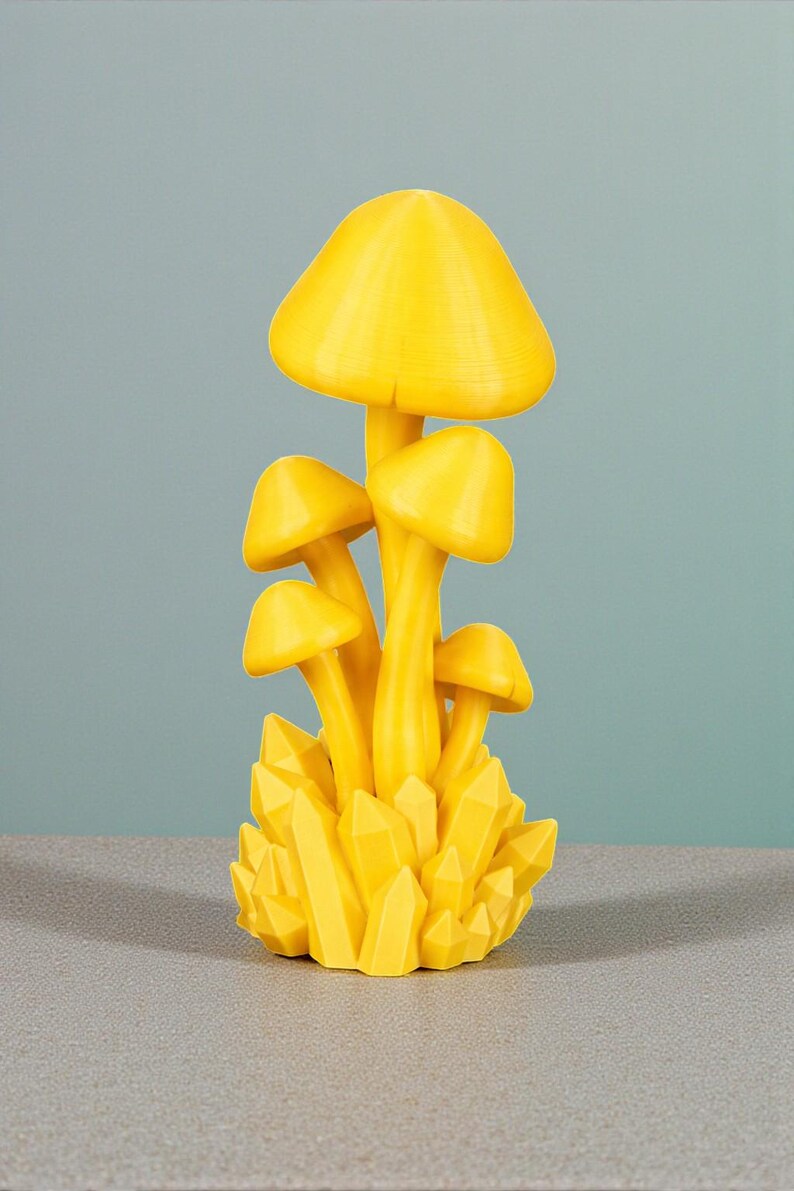 K&ouml;nnte beinhalten: Eine leuchtend gelbe Pilzskulptur mit mehreren Pilzkappen und -stielen, auf einem Sockel aus gelben kristallartigen Formationen. Es handelt sich um einen Dekorationsartikel, wahrscheinlich f&uuml;r die Inneneinrichtung.