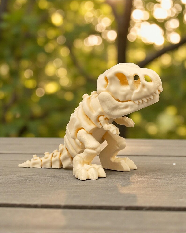 May include: A cream-colored dinosaur skeleton figurine. The toy dinosaur has a detailed skeletal structure, including ribs, spine, and skull. The figurine is posed in a standing position with its arms at its sides. The background is blurred, with green foliage and sunlight.