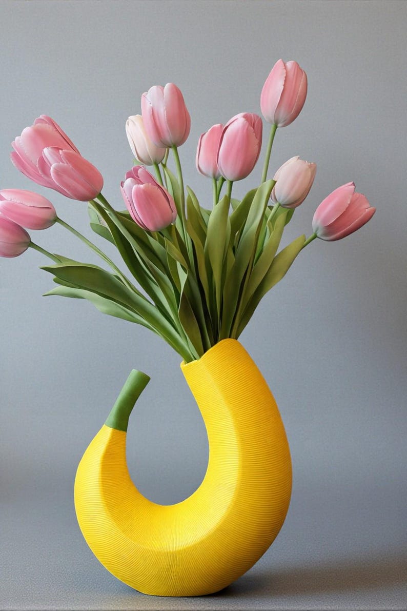 May include: A unique yellow vase shaped like a banana, holding a bouquet of pink tulips with green stems and leaves. The vase has a textured surface and a curved design, set against a gray background.