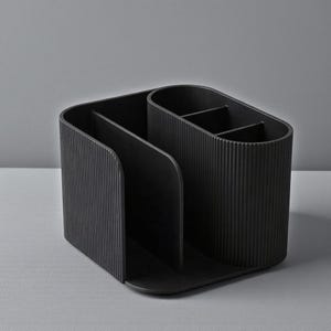 May include: A black desk organizer with multiple compartments. The organizer has a rectangular base and a curved design with vertical ribbed detailing. It is designed to hold pens, pencils, and other office supplies.