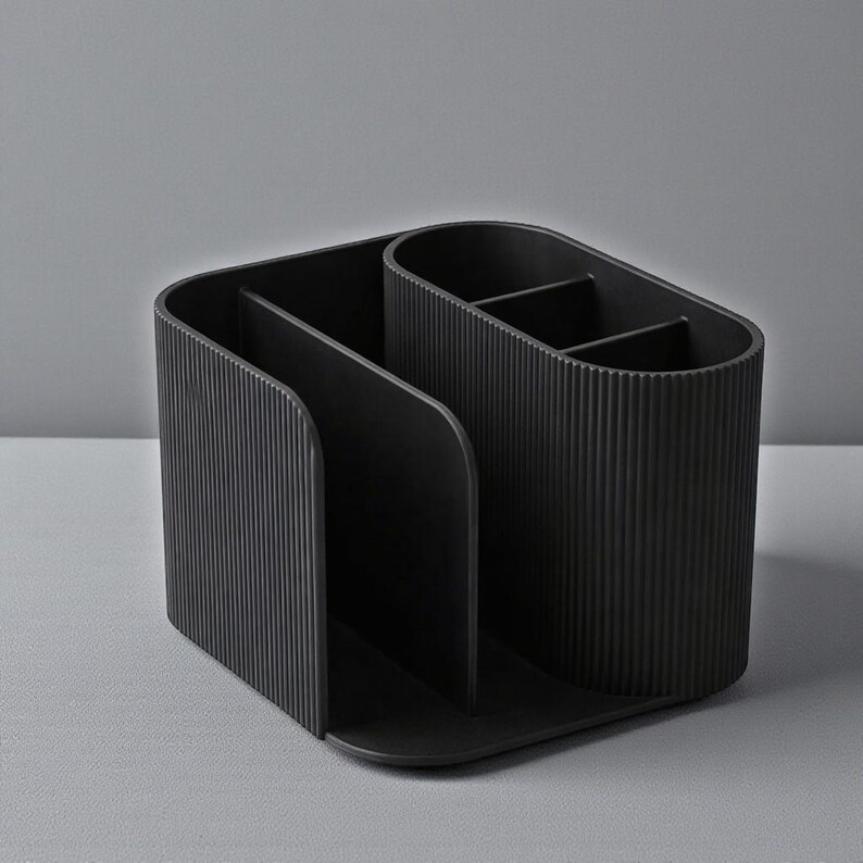 May include: A black desk organizer with multiple compartments. The organizer has a rectangular base and a curved design with vertical ribbed detailing. It is designed to hold pens, pencils, and other office supplies.