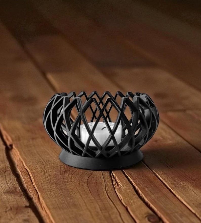 May include: A black, geometric candle holder with a white candle inside. The holder has a round base and an open, lattice-like design. The candle holder is made of metal and sits on a wooden surface.