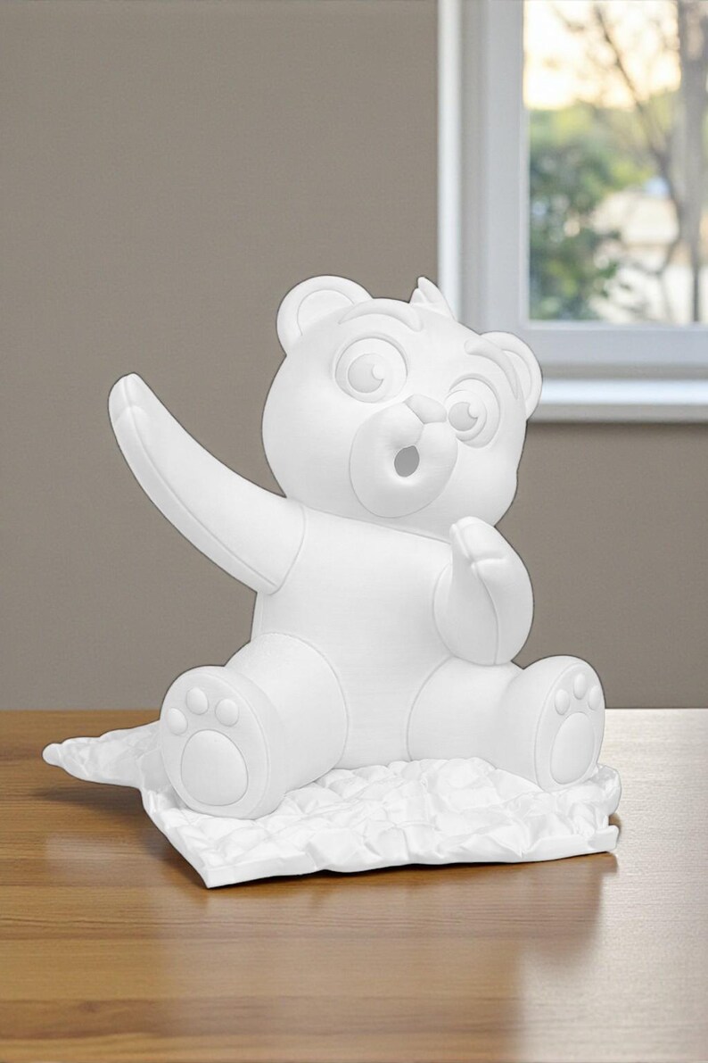 May include: A white, cartoon-style bear figurine with outstretched arm and open mouth. The bear is sitting on a textured, white surface. The figurine has large eyes and a friendly expression, suggesting a playful theme.