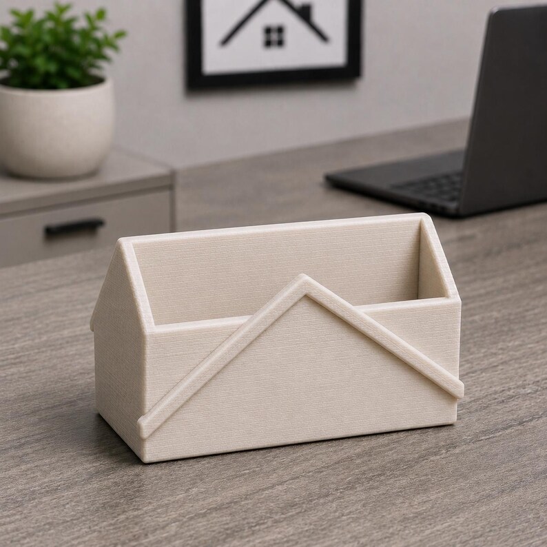 Pu&ograve; includere: Un organizer da scrivania beige a forma di casa. L'organizer ha una base rettangolare e un design a tetto spiovente. L'organizer a forma di casa &egrave; realizzato in un materiale strutturato e poggia su una scrivania di legno.