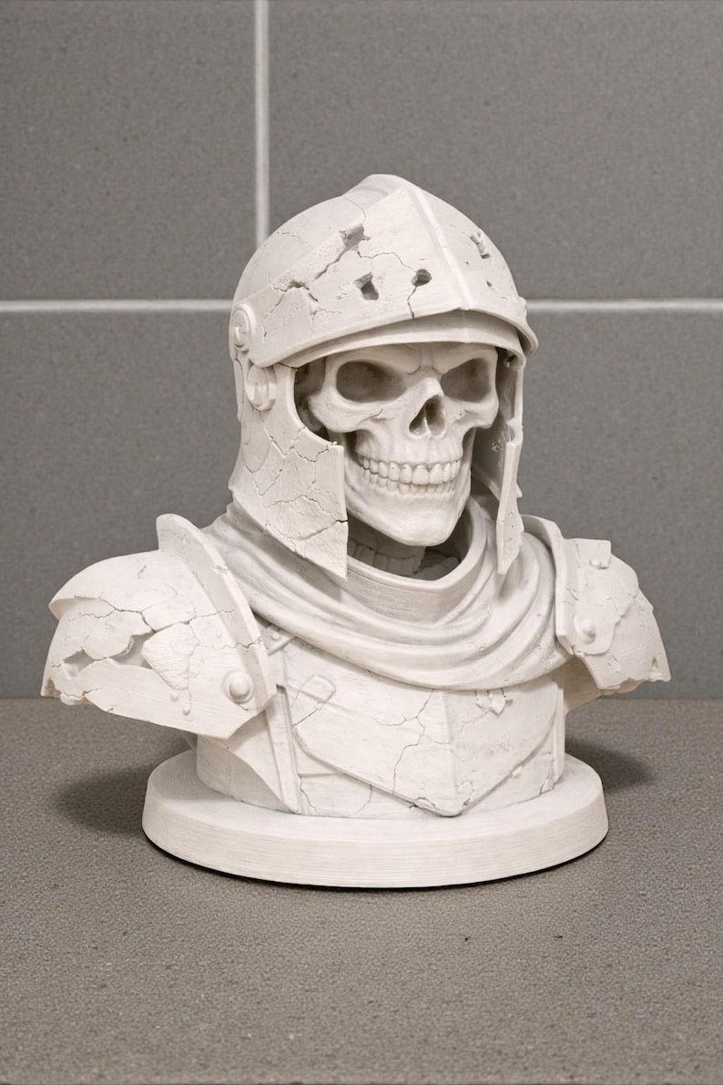May include: A white bust of a skeleton wearing a cracked, weathered helmet and armor. The sculpture features a detailed skull and is mounted on a circular base, showcasing a gothic or fantasy theme.