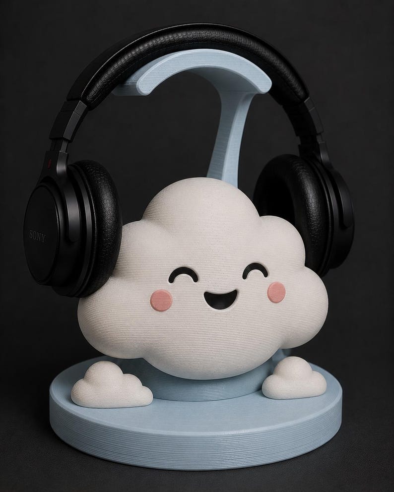 May include: A white cloud-shaped headphone stand with a smiling face and pink cheeks. The stand holds a pair of black headphones. The base and support are light blue. The headphones are black and have the brand name "SONY" printed on them.