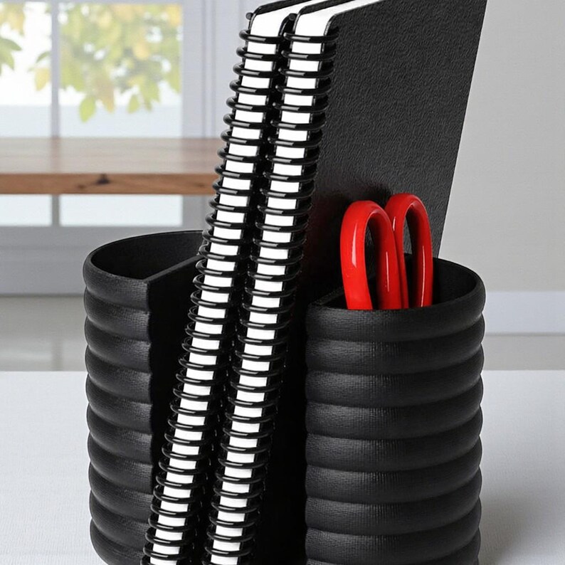 May include: A black desk organizer with a ribbed design, holding two spiral-bound notebooks and a pair of red scissors. The organizer has three compartments, providing storage for office supplies. The notebooks have white pages and black covers.