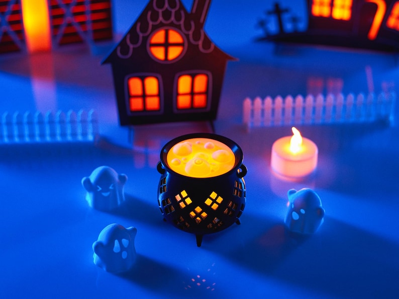 May include: A black cauldron with a glowing orange liquid inside, surrounded by three white ghost figurines and a small white candle on a blue surface.