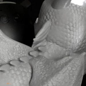 May include: A close-up of a white, textured sculpture of a dragon's head and part of its body. The sculpture has a detailed, scale-like pattern and a horn. The dragon's head is angled towards the left, with a wing-like structure visible.