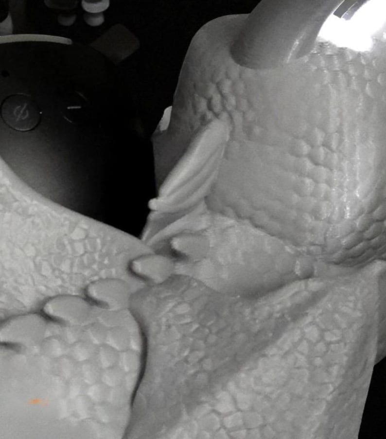 May include: A close-up of a white, textured sculpture of a dragon's head and part of its body. The sculpture has a detailed, scale-like pattern and a horn. The dragon's head is angled towards the left, with a wing-like structure visible.