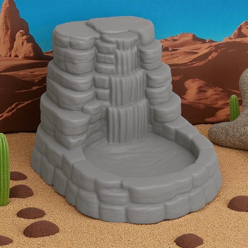 Puede incluir: Una escultura de cascada gris escalonada con una cuenca. La cascada tiene m&uacute;ltiples niveles, que se asemejan a rocas apiladas. El fondo presenta un paisaje des&eacute;rtico con cielo azul y cactus.