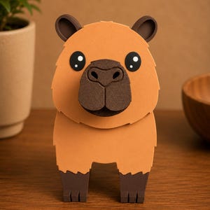May include: A handcrafted, three-dimensional capybara figure. The figure is primarily orange with dark brown accents on the ears, nose, and feet. The capybara has large, round eyes with white highlights. The figure is standing on a wooden surface.