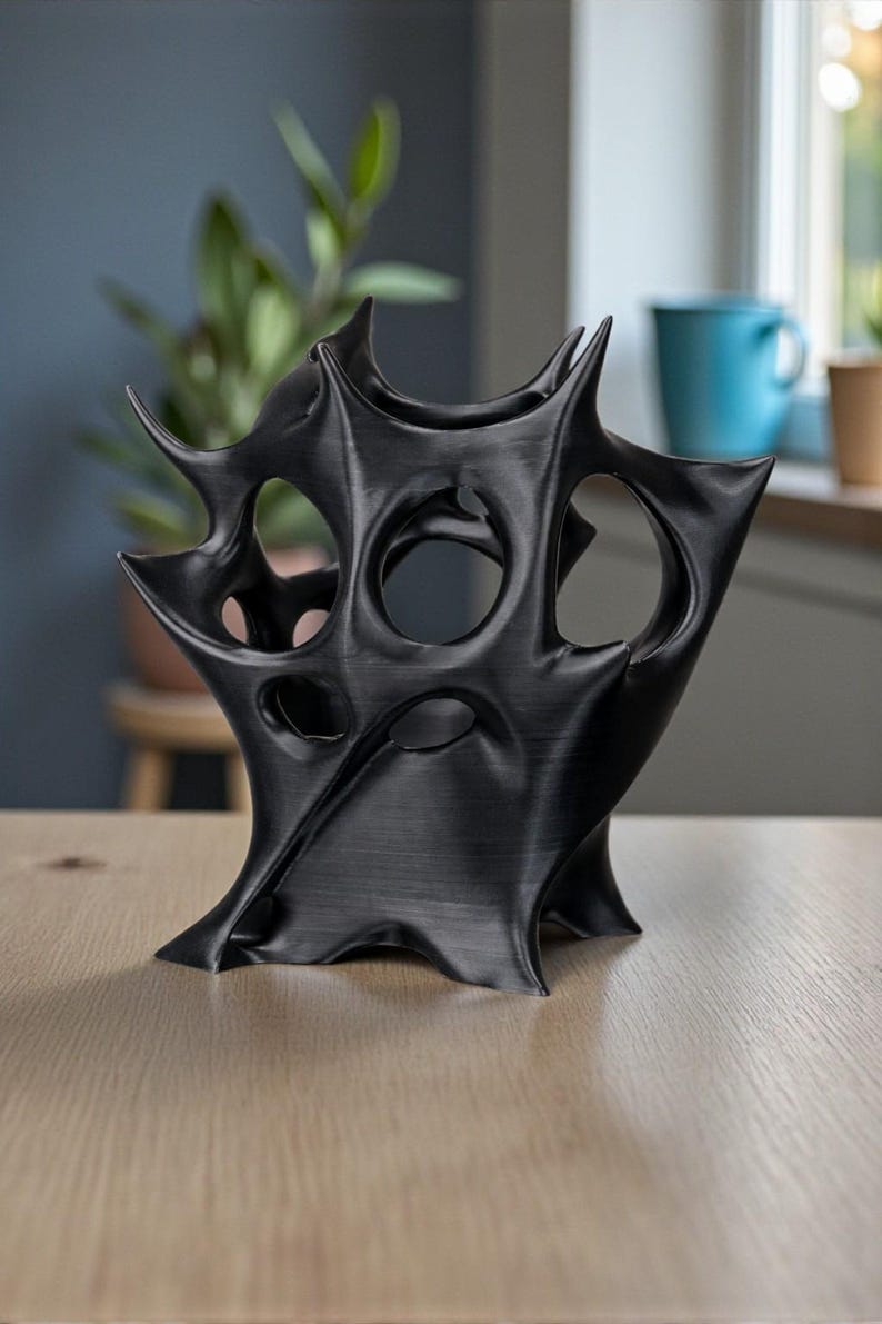 May include: A black, abstract sculpture with a complex, spiky design. The art piece has multiple openings and a textured surface. It is displayed on a light-colored wooden table, with a blurred background.