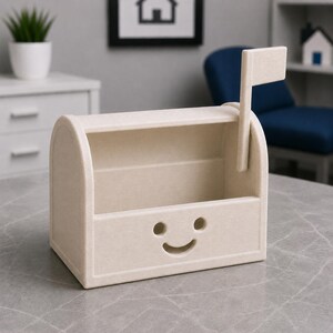 May include: A beige mailbox-style desk tidy with a smiling face design. It features a flag and is made from a textured material. The interior is open for storage of stationery or small items.