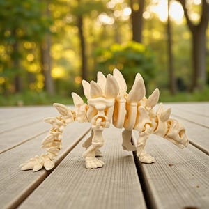 May include: A cream-colored, articulated dinosaur skeleton model. The model features a detailed design with visible ribs, a spiky back, and a long tail. It is posed on a wooden surface with a blurred background of trees.