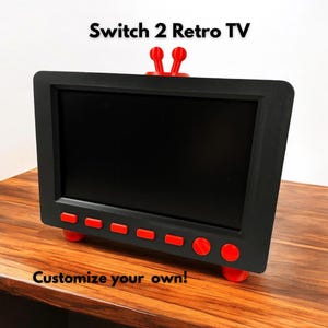 Puede incluir: Un televisor retro negro con detalles rojos, incluyendo la antena, los botones y los pies. La pantalla es negra, y el texto "Switch 2 Retro TV" y "Customize your own!" son visibles.