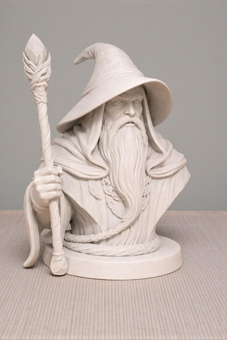 May include: A detailed white bust of a wizard with a long beard, a pointed hat, and a staff. The wizard's face has a stern expression. The staff has a crystal-like top. The bust is on a round base, and the wizard is wearing a robe.