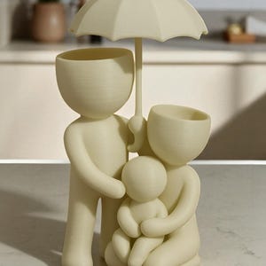 May include: A cream-colored family figurine with an umbrella. The sculpture depicts a family of four, with the parents holding the child. The heads of the parents are open, possibly for plants. The umbrella is held over the family.