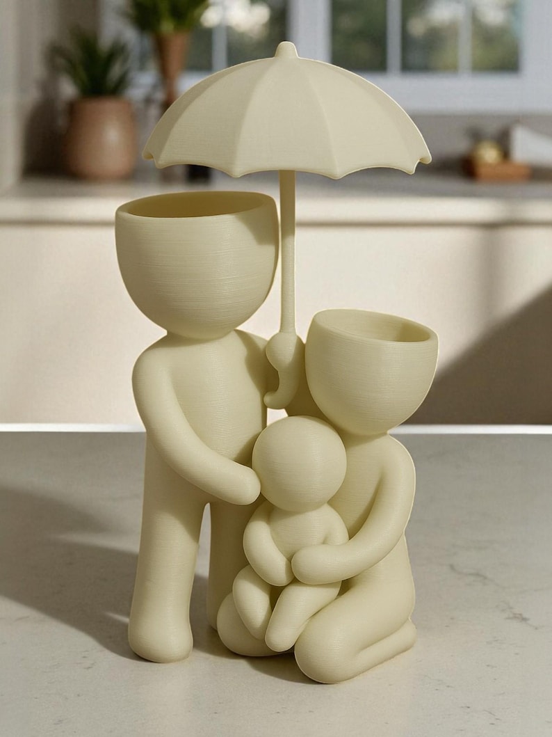 May include: A cream-colored family figurine with an umbrella. The sculpture depicts a family of four, with the parents holding the child. The heads of the parents are open, possibly for plants. The umbrella is held over the family.