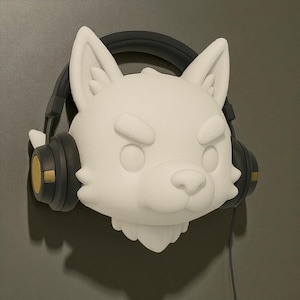 Könnte beinhalten: Eine weiße, stilisierte Wolfskopfskulptur mit schwarzen und goldenen Kopfhörern. Der Wolf hat einen strengen Ausdruck, mit gerunzelten Augenbrauen und leicht geöffnetem Mund. Die Kopfhörer haben goldene Akzente an den Ohrmuscheln und ein schwarzes Kabel hängt herunter.