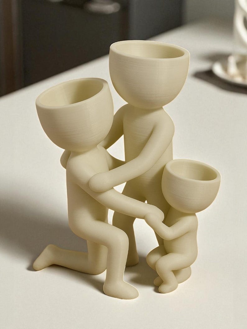 Op de afbeelding: Een cr&egrave;mekleurig familiebeeldje dat een knielende figuur, een staande figuur en een kleine zittende figuur afbeeldt, allemaal met afgeronde hoofden en vereenvoudigde lichamen. De figuren zijn in een gebaar van steun en verbinding met elkaar verweven.