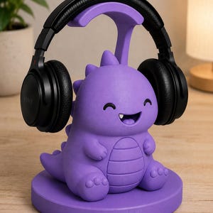 May include: A purple dinosaur-shaped headphone stand with a smiling face and black headphones resting on top. The stand is made of a solid material and sits on a round base. The headphones are black.